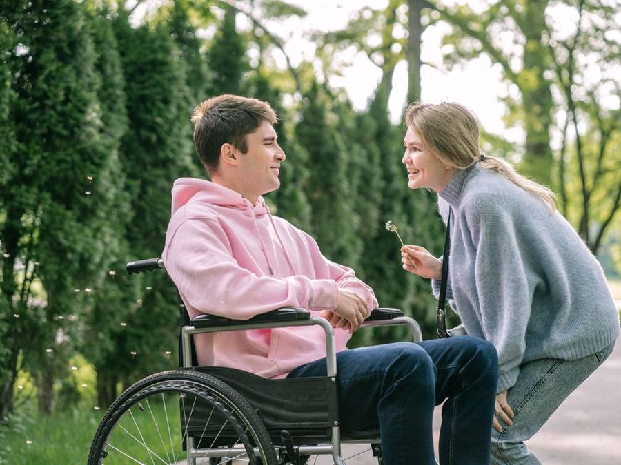 A young man in a wheelchair laughing with a friend in a park