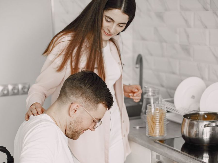 A support worker standing beside a man in a wheelchair as he prepares food in his kitchen