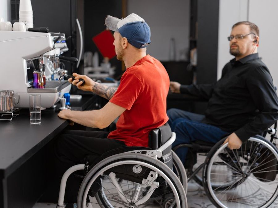 Two men who use wheelchairs working behind the counter of a café