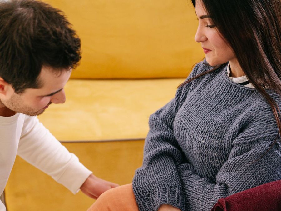 A support worker kneeling to help a woman in a wheelchair settle in at home